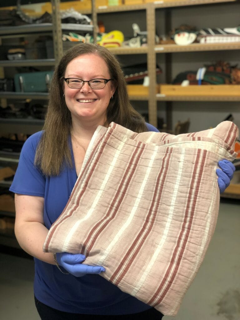 Collections Manager Megan Purcell holds the donation of a war time quilt that was made by Canadian women and sent to England.